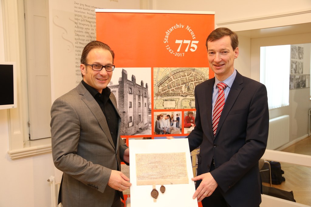 Bürgermeister Reiner Breuer und Stadtarchivleiter Dr. Jens Metzdorf mit einem Faksimile der Urkunde von 1242 mit der Ersterwähnung des Neusser Stadtarchivs