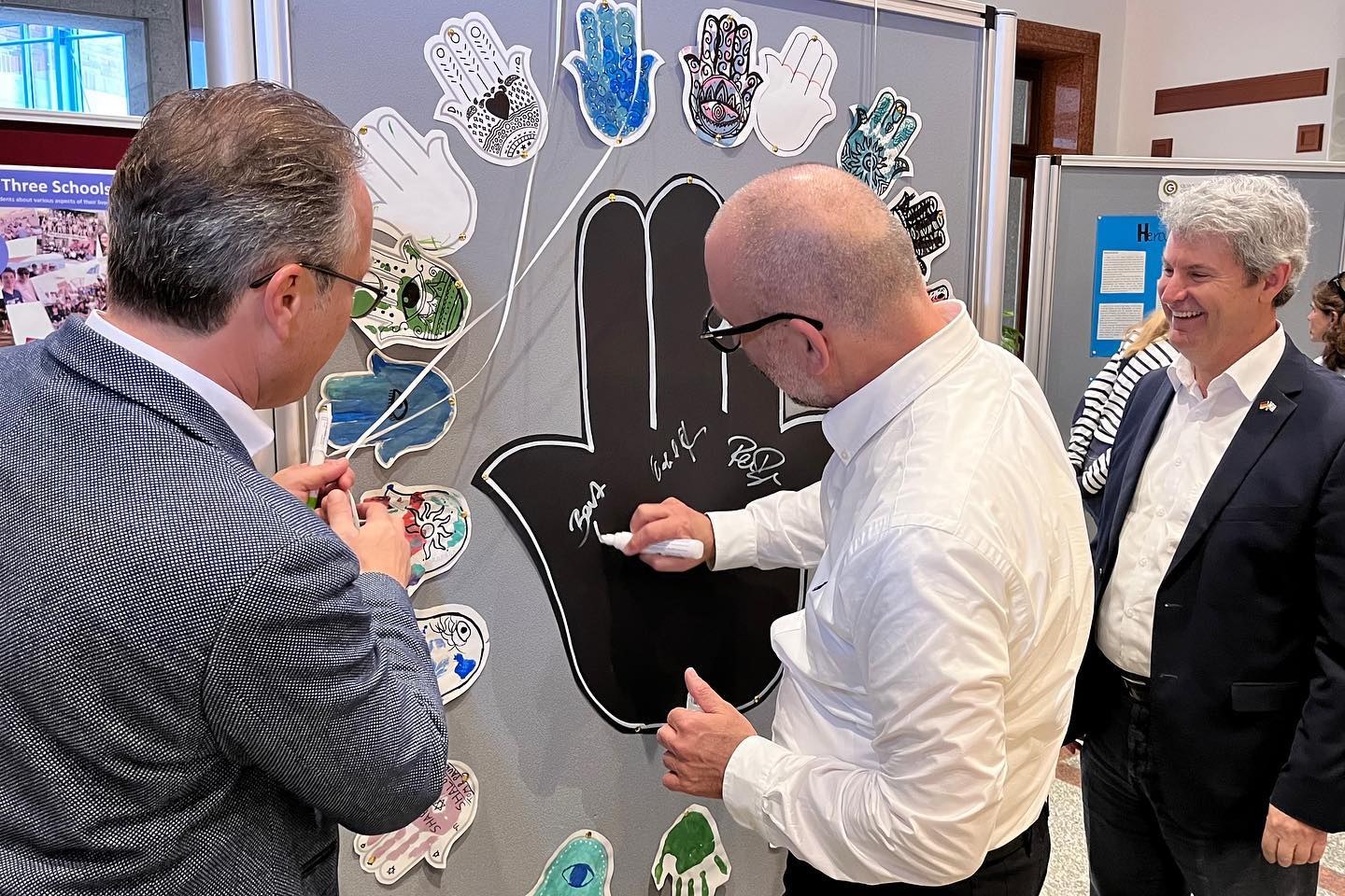 Bürgermeister Reiner Breuer, Bert Römgens und Dr. Oded Horowitz hinterlassen ihre Unterschriften auf der Ausstellung im Rathausfoyer.