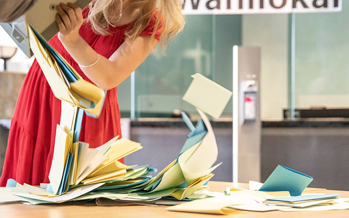 Eine Frau schüttet die Inhalte der Wahlurne einen Tisch, um mit der Auswählung der Briefwahlunterlagen zu beginnen.