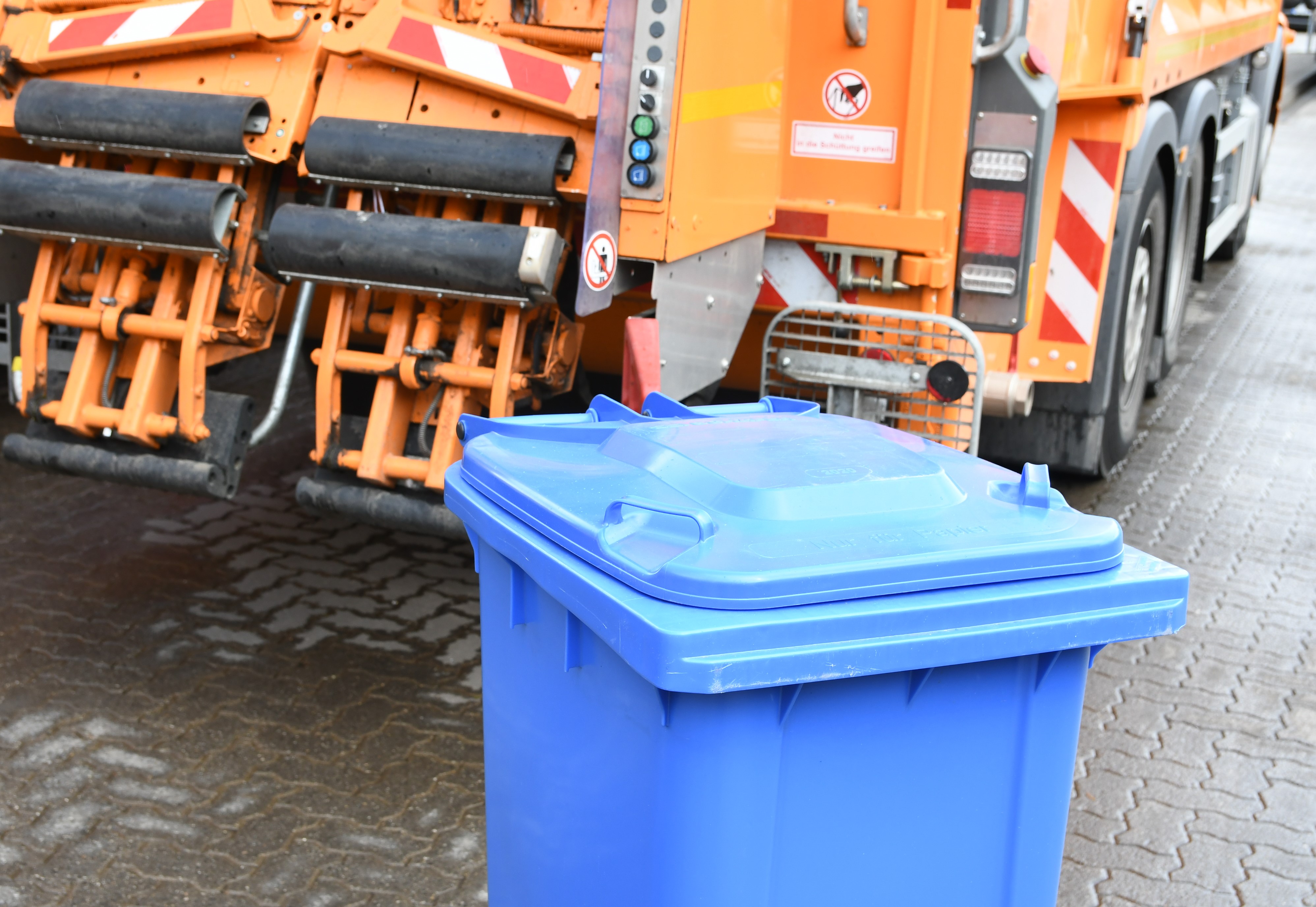 Blaue Mülltonne vor einem Fahrzeug der AWL