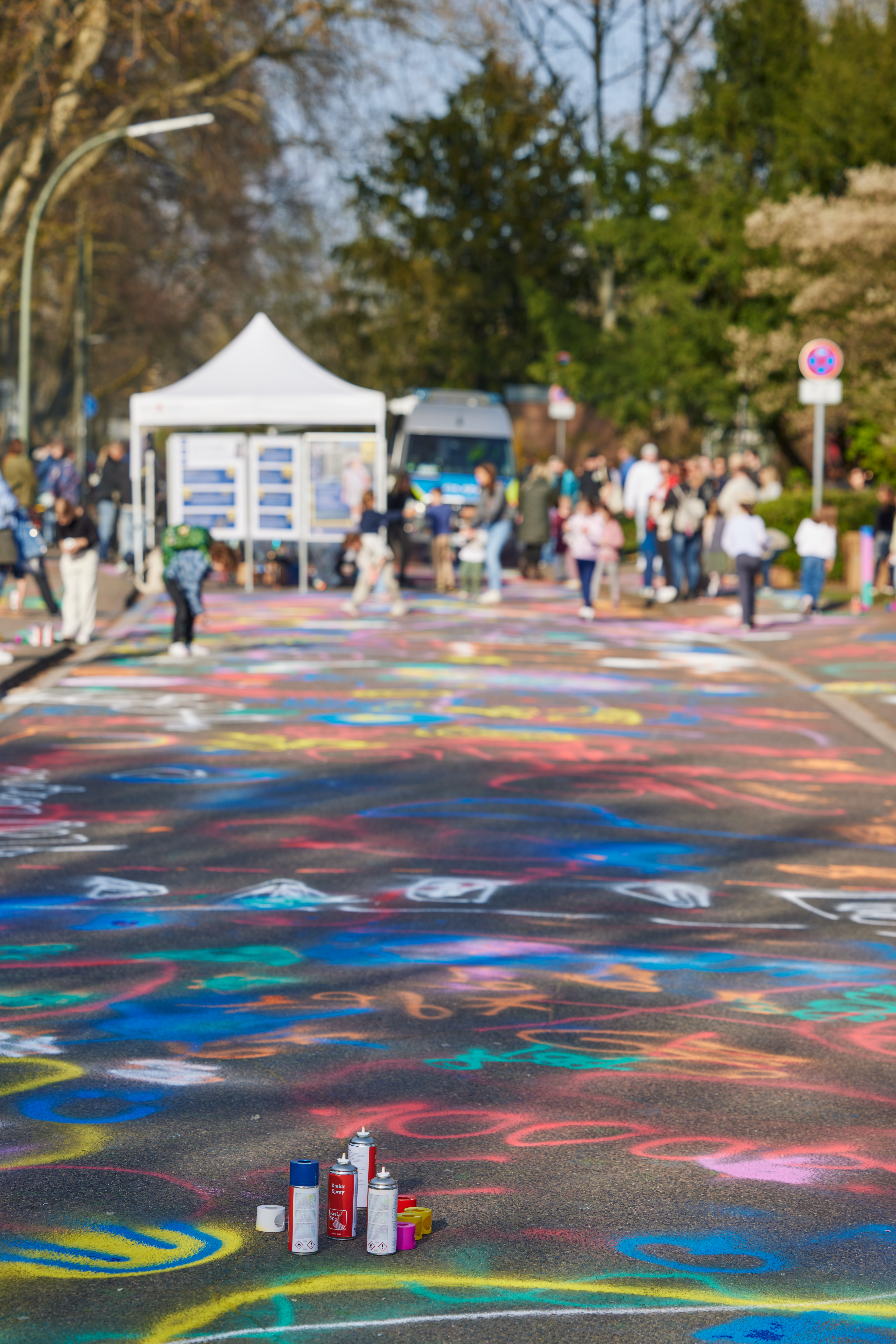 Straßenkunst mit Sprühdosen und buntem Graffiti im Freien, Menschen im Hintergrund.