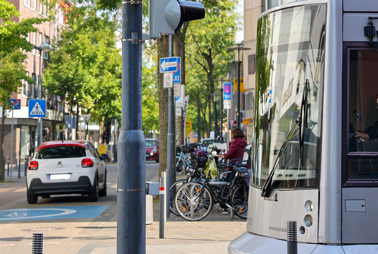 Straßenkreuzung in der Neusser City mit einem Auto, Fahrradständer und einer Straßenbahn.