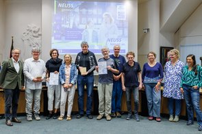 Eine Gruppe von Menschen wird im Ratssaal der Stadt Neuss ausgezeichnet und hält eine Urkunde in die Kamera.
