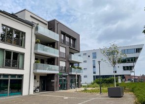 Zwei moderne Mehrfamilienhäuser mit Balkonen, eines hell verputzt, das andere mit dunklen Ziegeln versehen. Im Hintergrund ist das markante Kopfgebäude am Hafenbecken 1 mit seiner schrägen, an einen Schiffsbug erinnernden Frontseite zu erkennen.