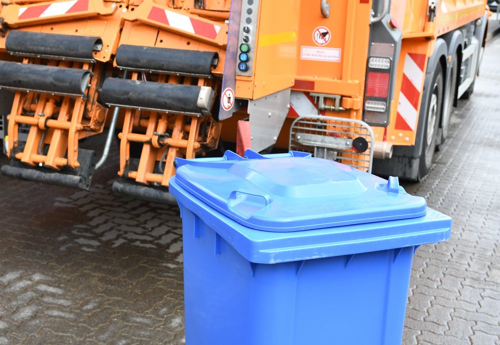 Blaue Mülltonne vor einem Fahrzeug der AWL