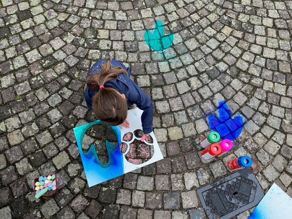 Kind von oben, dass den STraßenraum mit Sprühkreide verschönert und bunter macht