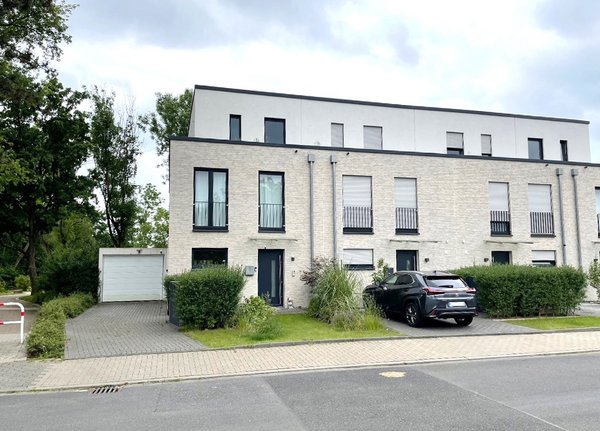 Frontansicht einer modernen Reihenhausanlage mit gepflegtem Vorgarten und Garage.