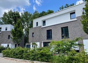 Zwei moderne Reihenhäuser mit zweifarbiger Fassade und einem Grünstreifen davor.