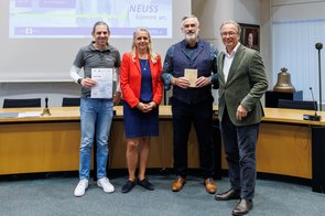 Eine Gruppe von Menschen wird im Ratssaal der Stadt Neuss ausgezeichnet und hält eine Urkunde in die Kamera.
