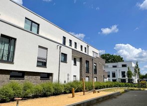 Modernes Wohngebäude mit zweifarbiger Fassade und einem schmalen Spielplatzstreifen vor.