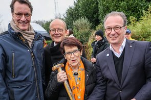 Prof. Dr. Rita Süssmuth steht zwischen den Herren Wüst und Breuer und hält einen Spaten in der Hand.