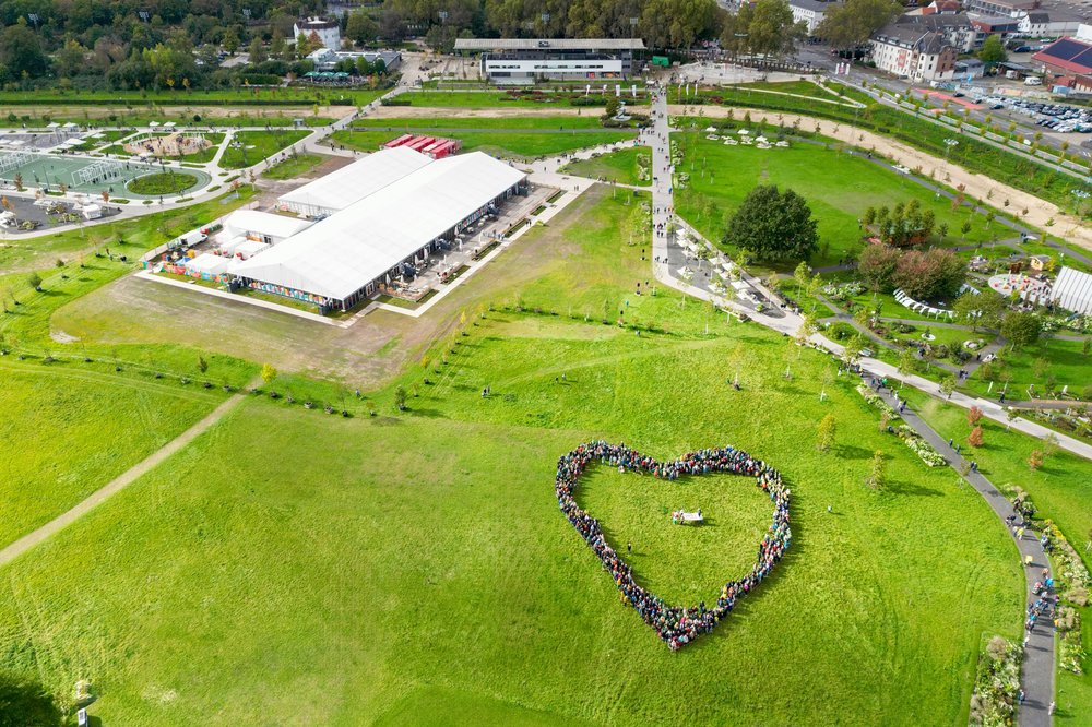 Drohnenfoto: Hunderte Menschen Bilden ein Herz auf dem Gelände der Landesgartenschau.