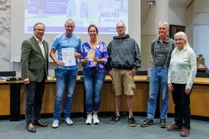 Eine Gruppe von Menschen wird im Ratssaal der Stadt Neuss ausgezeichnet und hält eine Urkunde in die Kamera.