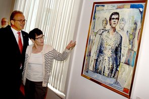 Frau Süssmuth zeigt auf ihr Portraitgemälde, auf dem eine junge Frau mit Brille und Frau Süssmuths markanter Frisur zu sehen ist: aufrecht stehend und scheinbar dabei, eine Rede anzustimmen.