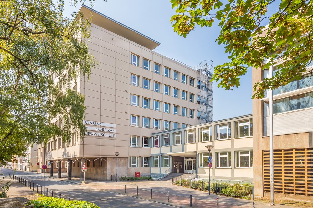 Außenansicht eines Schulgebäudes bei sonnigem Wetter eingerahmt von Bäumen.