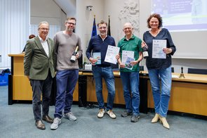 Eine Gruppe von Menschen wird im Ratssaal der Stadt Neuss ausgezeichnet und hält eine Urkunde in die Kamera.