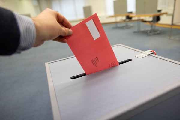 Ein roter Wahlschein wird im Wahlamt in eine Wahlurne geworfen.