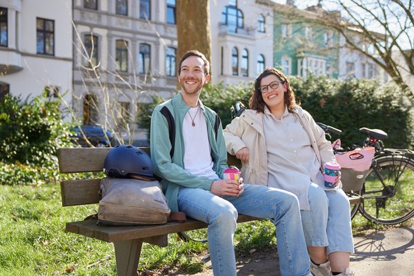 Zwei lächelnde Personen sitzen auf einer Bank und machen nach einer Fahrradtour eine Pause.