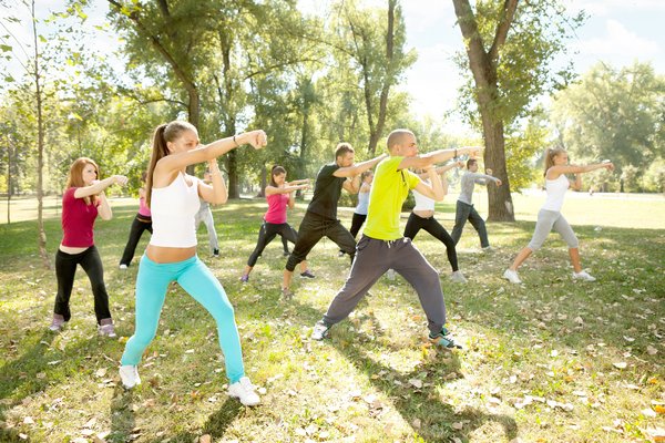 Eine Gruppe junger Erwachsener macht Boxübungen an einem sonnigen Tag im Park.