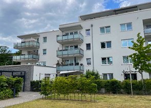 Rückansicht eines modernen Mehrfamilienwohnblocks mit Balkonen und einer Grünfläche.