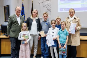 Eine Gruppe von Menschen wird im Ratssaal der Stadt Neuss ausgezeichnet und hält eine Urkunde in die Kamera.