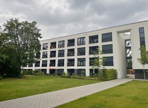 Moderner, mehrstöckiger Gebäudekomplex mit großen Fensterflächen und einem markanten Durchgangsbereich.