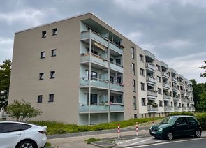 Modernes Wohnhausblock mit Balkonen, davor parkende Autos.