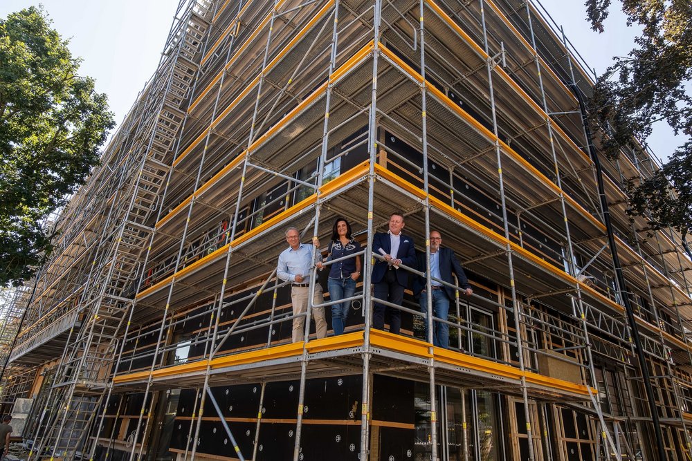 Vier Personen stehen auf einem Gerüst vor einem Gebäude, das renoviert wird.