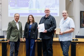 Eine Gruppe von Menschen wird im Ratssaal der Stadt Neuss ausgezeichnet und hält eine Urkunde in die Kamera.