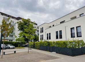 Wohngebiet mit Parkplatz, Bäumen, Sitzbank und mehreren modernen Wohnhäusern.