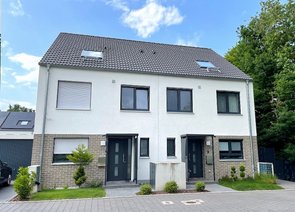 Freistehendes Doppelhaus mit weiß verputzten Wänden und geklinkerten Akzenten. Daneben ist eine Garage erkennbar.