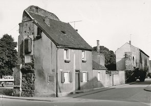 Schwarz-weiß-Foto eines Wohnhauses, welches in einen Stützbogen des Hamtors übergeht. In diesen Bogen eingelassen ist ein Glaskasten.