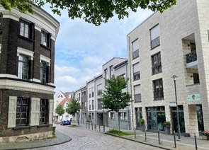 Markante Straßenecke mit Kopfsteinpflasterweg und modernen Gebäuden auf der rechten sowie einem historischen Gebäude auf der linken Seite.