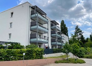 Seitlicher Blick auf einen Mehrfamilienwohnblock mit Balkonen und bepflanzter Umgebung.