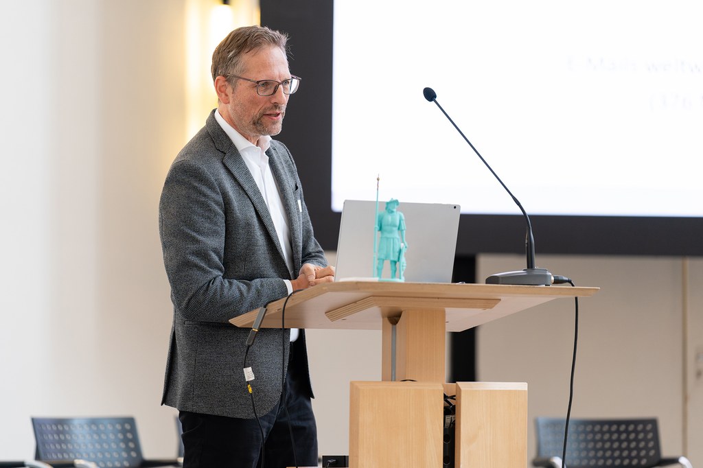 Prof. Linus Schleupner von der Rheinischen Fachhochschule steht am Pult und hält einen Vortrag.